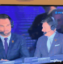 a tv screen shows two men wearing headphones and a name tag that says dave gooucher