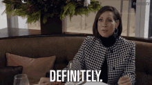 a woman sits at a table with a glass of wine and says " definitely "