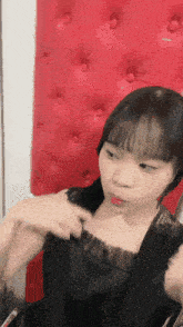 a girl in a black dress is sitting in front of a red cushioned wall