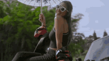 a woman is sitting on the back of a motorcycle holding an umbrella and smiling .
