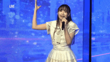 a girl in a white dress is singing into a microphone while standing in front of a blue screen .