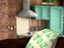 a green and white pillow on a couch with a kitchen in the background