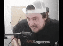 a man wearing a hat and a t-shirt is standing in front of a microphone .