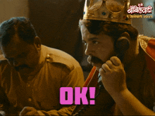 a man with a crown on his head is talking on a phone and the word ok is on the bottom