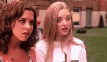 two women are standing next to each other in a grassy field and looking at each other .
