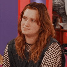 a woman with long red hair wearing a black tank top with fishnet sleeves