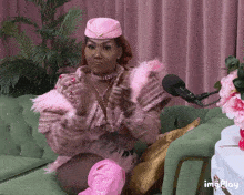 a woman in a pink outfit is sitting on a green couch next to a microphone and flowers