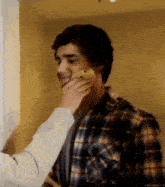 a man in a plaid shirt is getting a banana on his face .