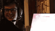 a man wearing headphones and glasses is smiling in front of a computer screen
