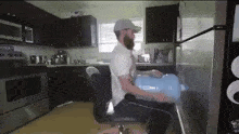 a man is sitting in a chair in a kitchen holding a blue water cooler