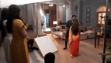 a man and a woman are standing in a living room . the woman is wearing a red saree .