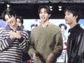three young men are standing next to each other on a stage and one of them is wearing a green sweater