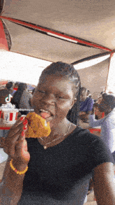 a woman in a black shirt is eating a piece of chicken