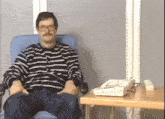 a man wearing glasses and a striped shirt sits in a chair