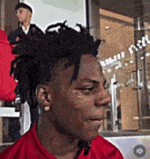 a young man with dreadlocks is crying and wearing a red shirt and earrings .