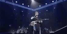 a man is playing a guitar on a stage in front of a crowd .