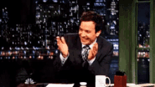 a man in a suit and tie is sitting at a desk with his hands on his face .