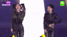 two women are standing on a stage and one is singing into a microphone and the other is dancing .