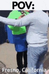 a man in a white sweater is hugging a woman in a green vest in fresno california .