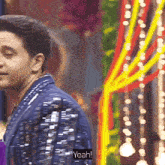 a man in a blue sequined jacket is standing in front of a colorful background and says yeah .