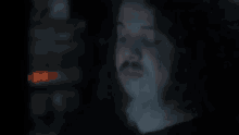 a man with long curly hair and a beard is smoking a cigarette in the dark .