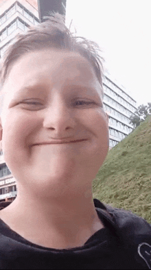 a young boy is smiling and making a funny face while standing in front of a building .