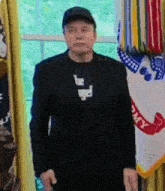 a man wearing a black suit and a black hat is standing in front of a flag