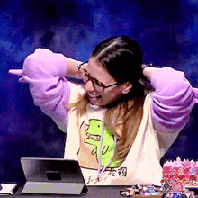 a woman wearing purple gloves and a t-shirt with a dinosaur on it is sitting in front of a tablet