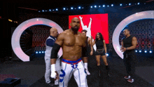 a group of wrestlers are standing on a stage in front of a large screen with a man in the air on it