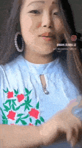 a woman wearing a blue shirt with flowers on it and hoop earrings