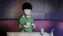 a boy in a green hoodie is sitting at a table with a drink and a toy .