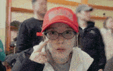 a woman wearing glasses and a red hat has her finger on her ear