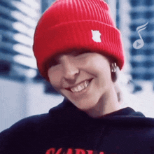 a woman wearing a red beanie and a black hoodie smiles for the camera