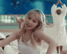 a woman in a white dress is dancing on a bed with a man in a bathrobe standing behind her .