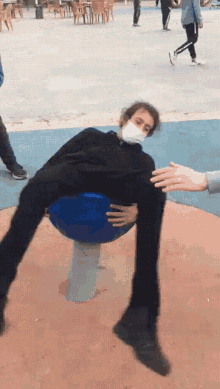 a man wearing a mask is sitting on a blue ball with his legs crossed