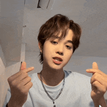 a young man wearing a blue shirt and a chain necklace is giving a thumbs up