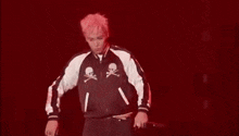 a man with pink hair is wearing a black and white jacket with skulls on it and is dancing on a stage .