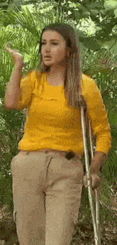 a woman in a yellow shirt is walking with crutches in the woods .