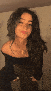 a woman in a black off the shoulder top and green pants is standing in front of a wall
