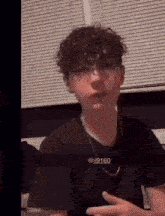 a young man with curly hair is wearing glasses and a black shirt .