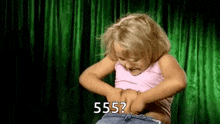a little girl is standing in front of a green curtain holding her belly and asking .