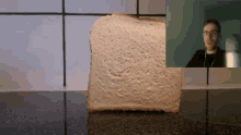 a slice of bread is sitting on a counter next to a man wearing glasses