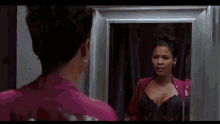 a woman is looking at herself in a mirror in a bra .