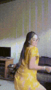 a woman in a yellow dress is dancing in a living room with a tv in the background .