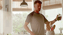 a man is standing in a kitchen holding a glass of green juice