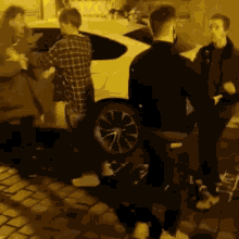 a group of men are standing around a car on a cobblestone street at night .
