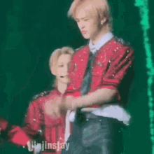 a man in a red shirt and tie is standing next to another man in a black shirt and tie on a stage .