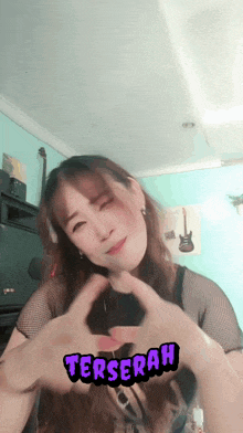 a woman is making a heart shape with her hands and the word terserah is visible behind her