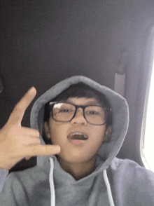 a young boy wearing glasses and a grey hoodie is giving a peace sign