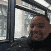 a man is smiling while sitting on a bus with a sign on the window that says sp